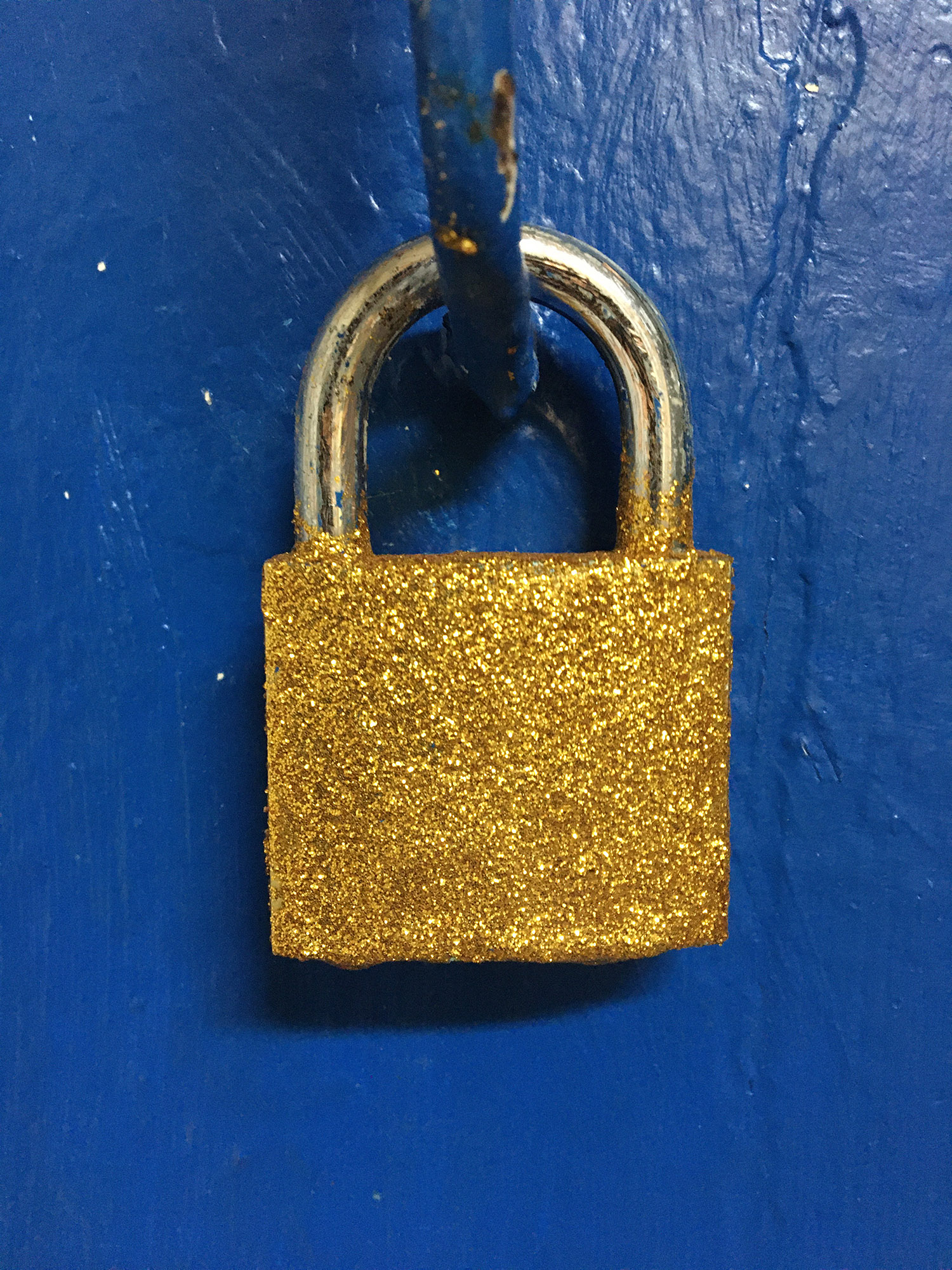 Un cadenas est accroché sur uen porte bleue. Il est recouvert de paillettes dorées.
